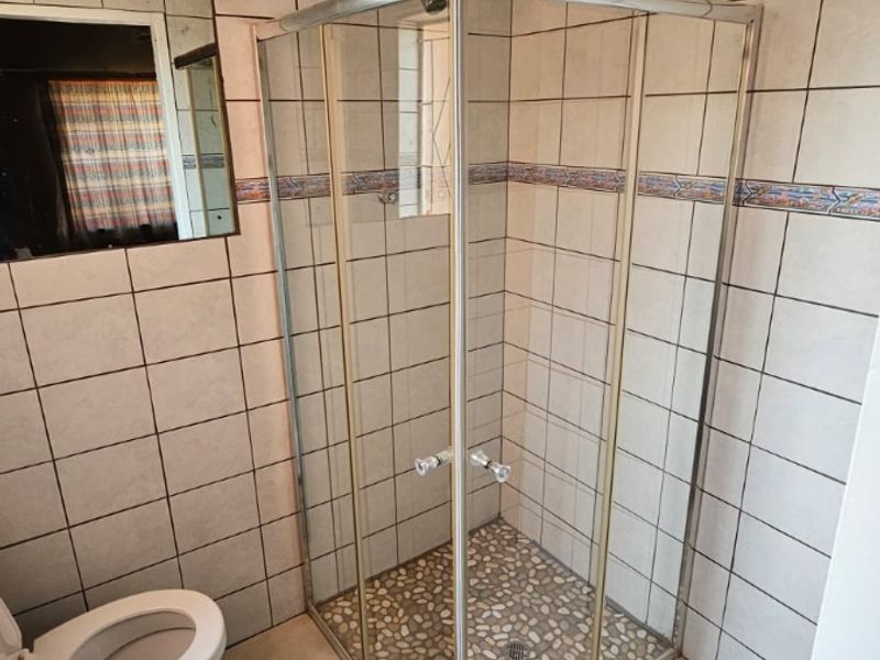 A functional bathroom featuring a corner shower enclosure with a pebble floor, ceramic wall and floor tiling, and a wall-mounted mirror.