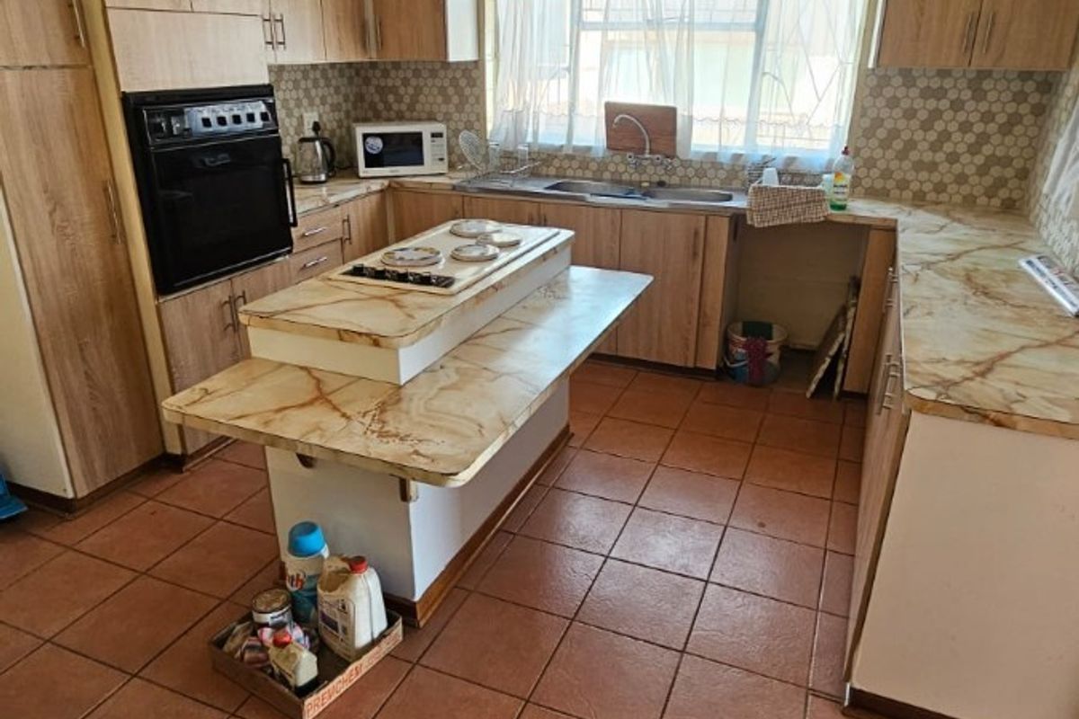 A functional kitchen featuring built-in cabinetry, a central island with a hob, and tiled flooring, offering potential for a modern renovation.