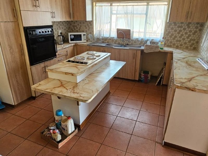 A functional kitchen featuring built-in cabinetry, a central island with a hob, and tiled flooring, offering potential for a modern renovation.