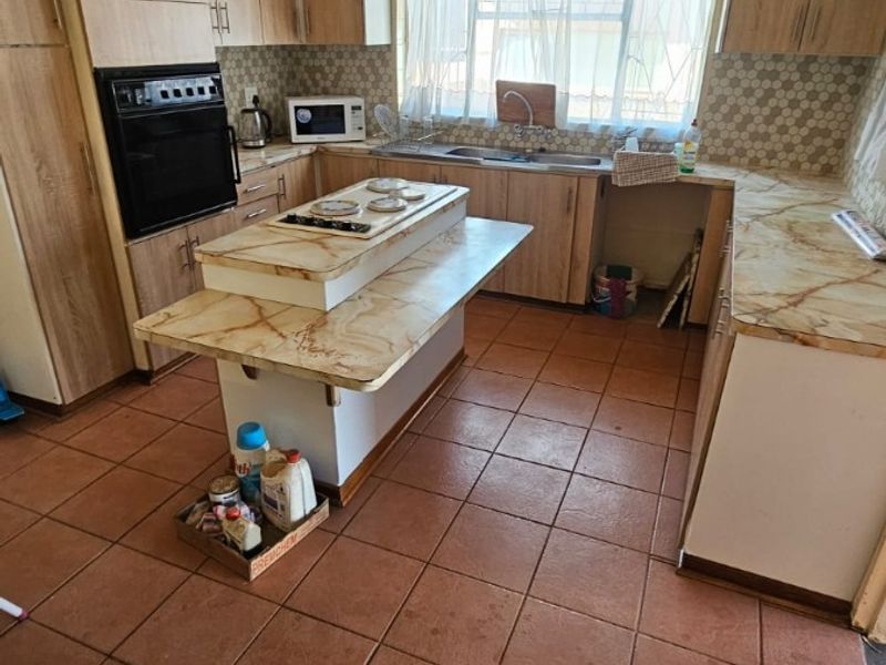 A functional kitchen featuring built-in cabinetry, a central island with a hob, built-in oven, and tiled flooring throughout.