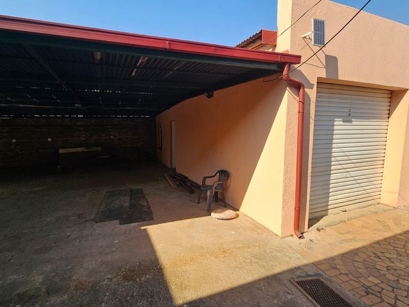 A spacious covered garage area featuring a roller shutter door, concrete flooring, and a corrugated metal roof structure.