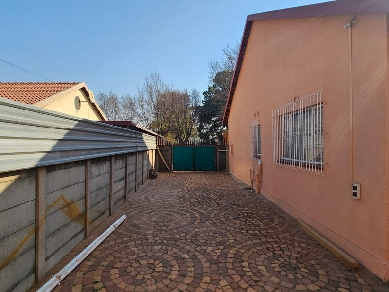 A side exterior view of the property featuring a paved driveway, secure boundary walling, and security gates.
