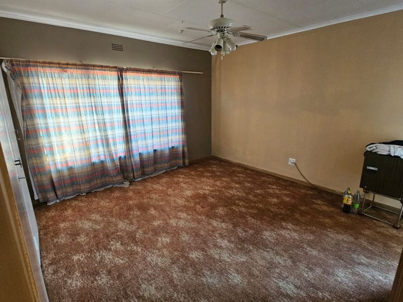 A spacious bedroom featuring carpeted flooring, a ceiling fan, and large windows with curtain rails, offering a blank canvas for renovation.