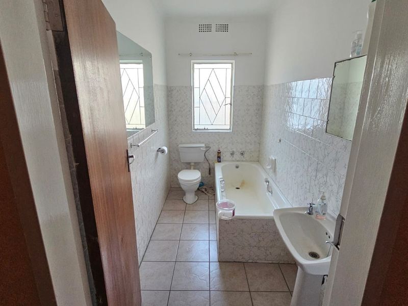 A functional bathroom featuring a bathtub, pedestal basin, and toilet with tiled finishes, offering potential for modernization and cosmetic updates.