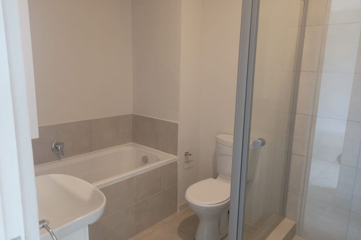 A clean, functional bathroom featuring a built-in bathtub, separate shower enclosure, toilet, and pedestal sink with neutral wall and floor tiling.