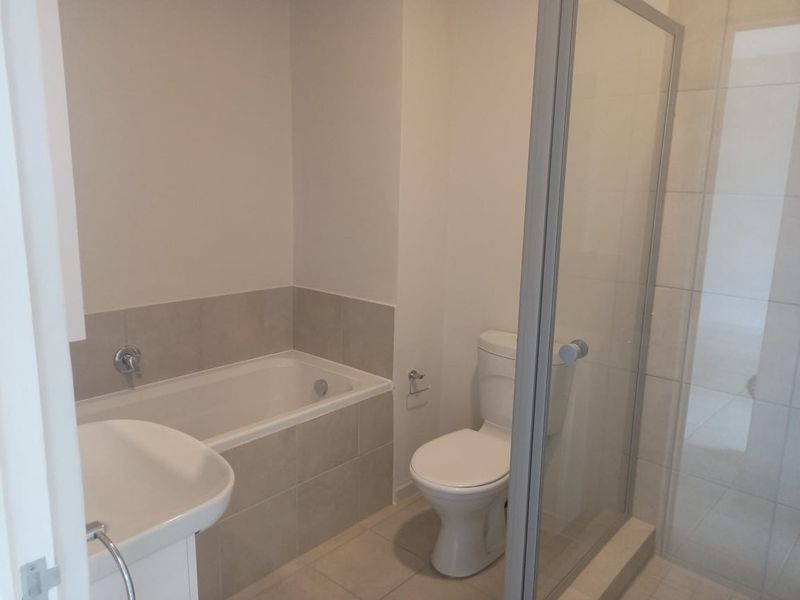 A clean, functional bathroom featuring a built-in bathtub, separate shower enclosure, toilet, and pedestal sink with neutral wall and floor tiling.