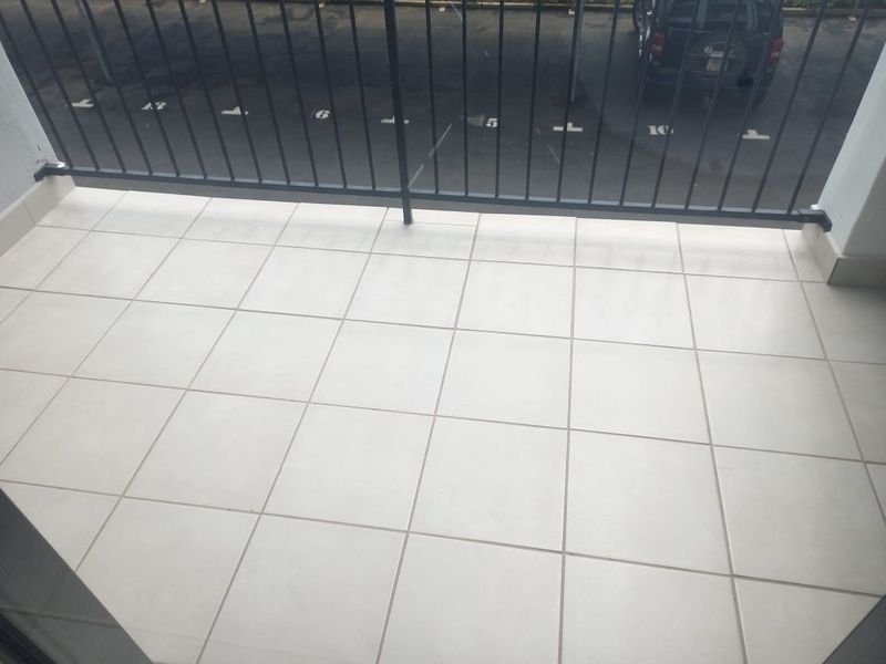 A clean, tiled balcony featuring a black metal balustrade overlooking a parking area.