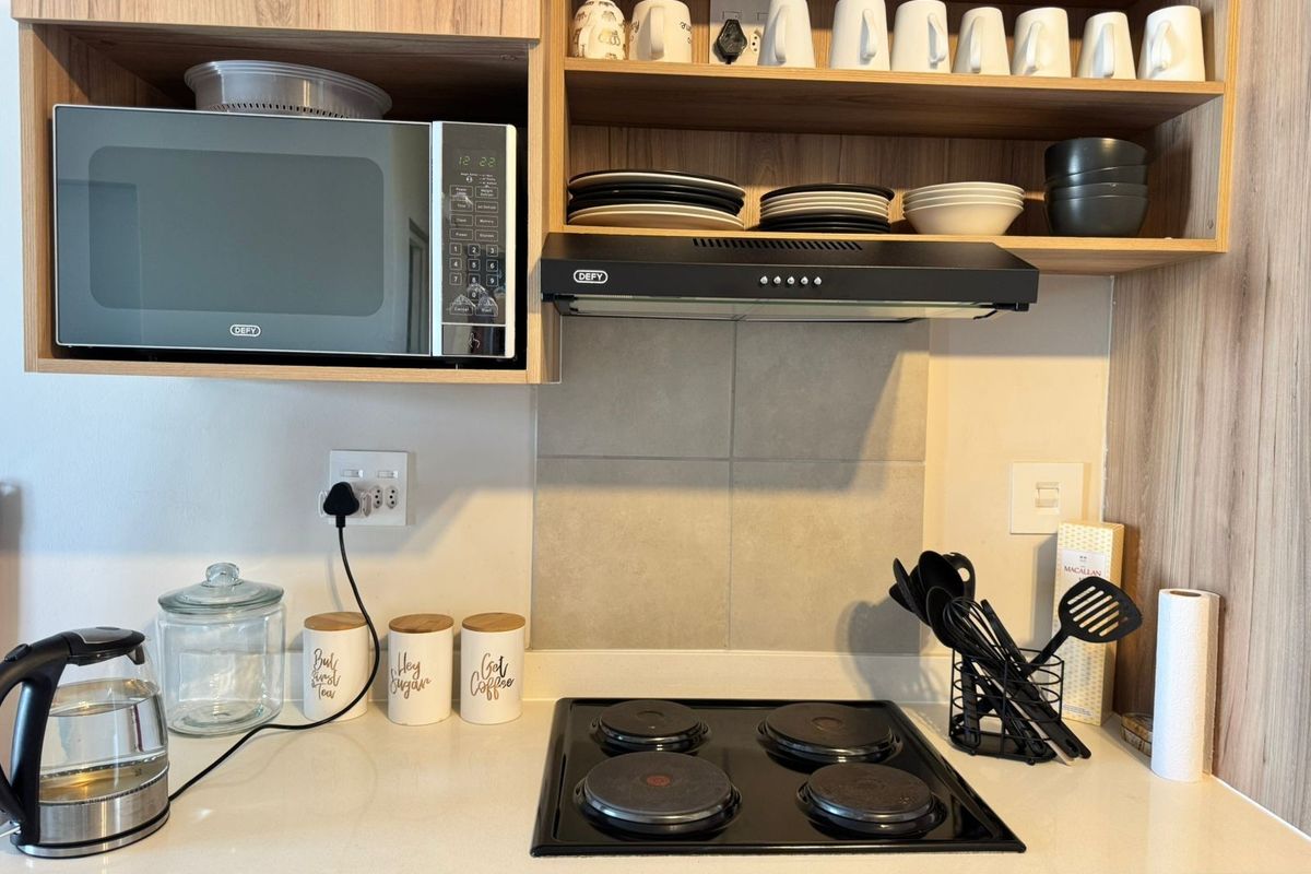 A modern kitchen workspace featuring a built-in microwave, electric hob, extractor fan, and clean laminate cabinetry with stone countertops.
