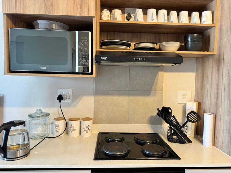 A modern kitchen workspace featuring a built-in microwave, electric hob, extractor fan, and clean laminate cabinetry with stone countertops.