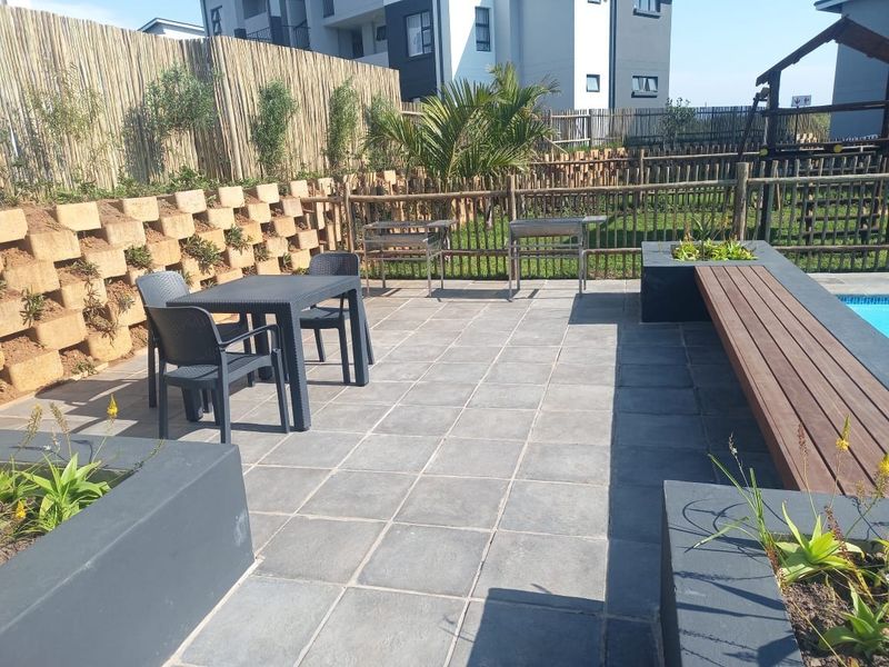 Outdoor pool area featuring a paved patio, built-in timber bench, integrated planters, and retaining wall, set within a fenced garden space.