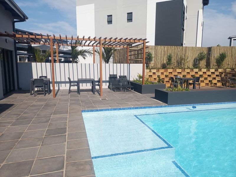 A well-maintained outdoor pool area featuring a tiled deck, timber pergola, and raised planter boxes, providing a pleasant space for relaxation.