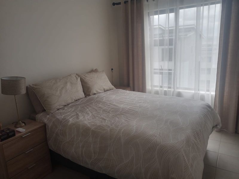 A functional bedroom featuring tiled flooring and large windows with installed curtain tracks, providing natural light.