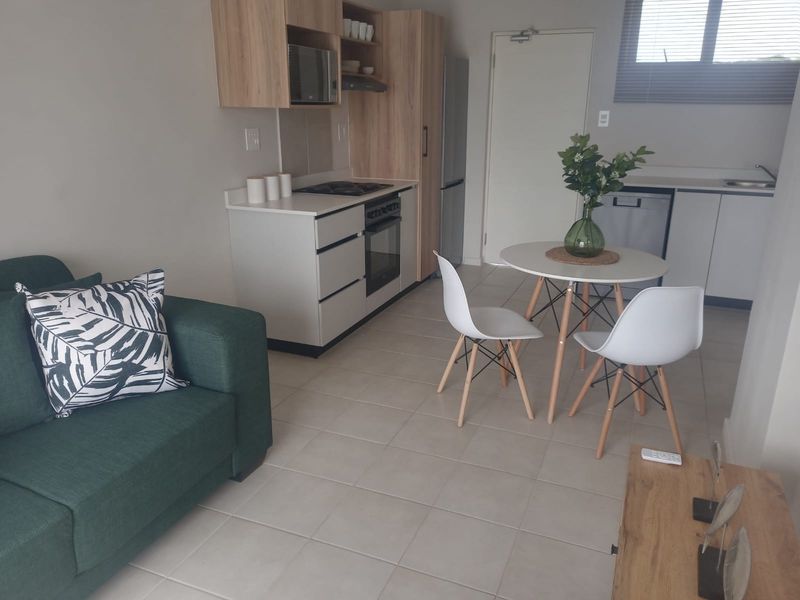 Modern open-plan living area featuring a compact kitchen with built-in cabinetry, electric hob, oven, and tiled flooring throughout.