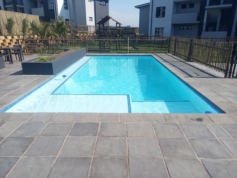A well-maintained swimming pool area featuring a tiled surround, built-in planter box, and secure timber perimeter fencing within a residential apartment complex.