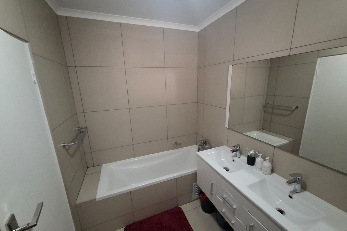 A functional bathroom featuring a built-in bathtub, a double vanity with integrated sinks, and neutral wall tiling.