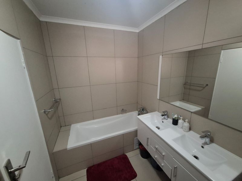 A functional bathroom featuring a built-in bathtub, a double vanity with integrated sinks, and neutral wall tiling.