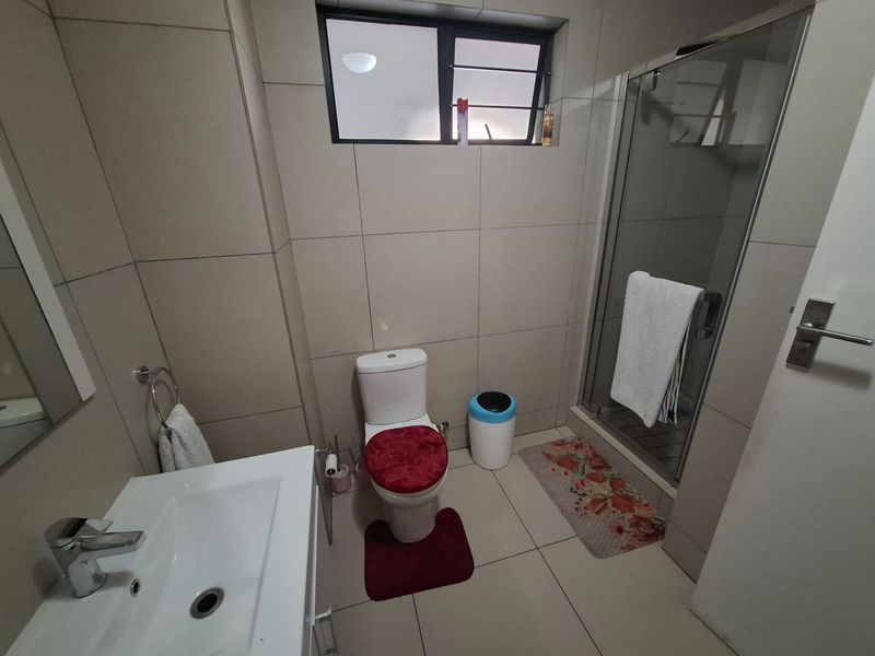 A functional bathroom featuring a glass-enclosed shower, modern vanity basin, and neutral floor-to-ceiling wall tiles.