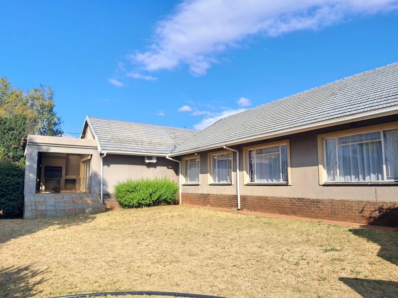 Rear view of the house featuring a tiled roof, brick base, and a covered patio area with a built-in braai.