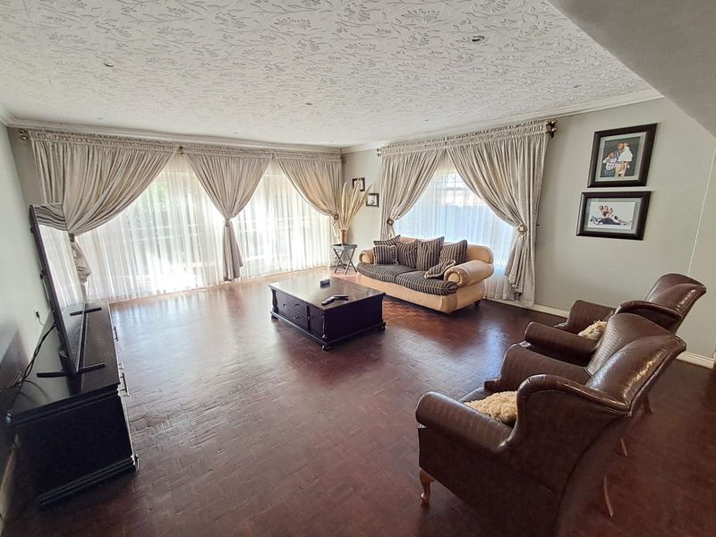 Spacious living room featuring classic parquet flooring, a decorative textured ceiling, and large windows with floor-to-ceiling curtains allowing for ample natural light.