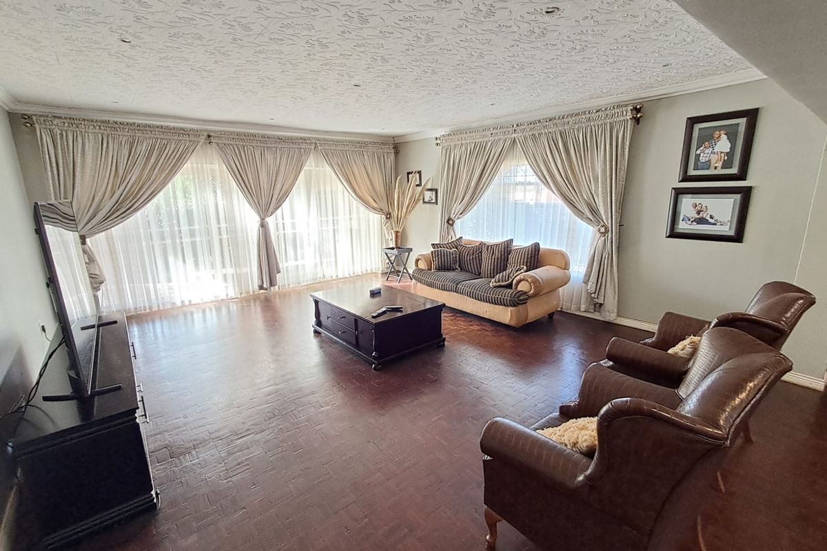 Spacious living room featuring classic parquet flooring, a decorative textured ceiling, and large windows with floor-to-ceiling curtains allowing for ample natural light.