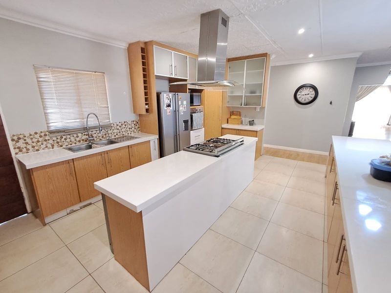 Spacious kitchen featuring a central island with gas hob, stainless steel extractor, stone countertops, and ample wooden cabinetry with a mosaic tile backsplash.