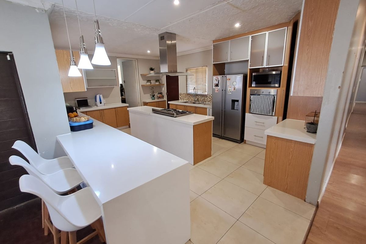 Modern kitchen featuring a central island with gas hob, stone countertops, built-in appliances, and ample cabinetry, finished with tiled flooring and contemporary lighting.