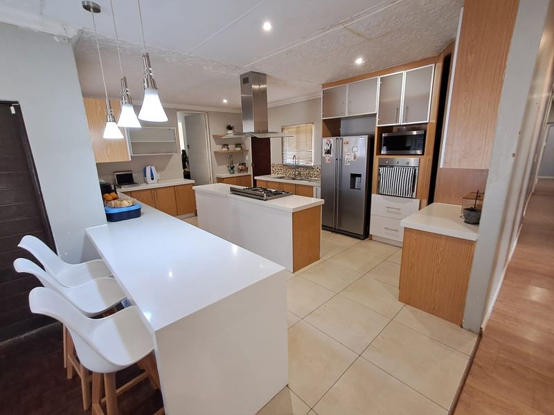 Modern kitchen featuring a central island with gas hob, stone countertops, built-in appliances, and ample cabinetry, finished with tiled flooring and contemporary lighting.