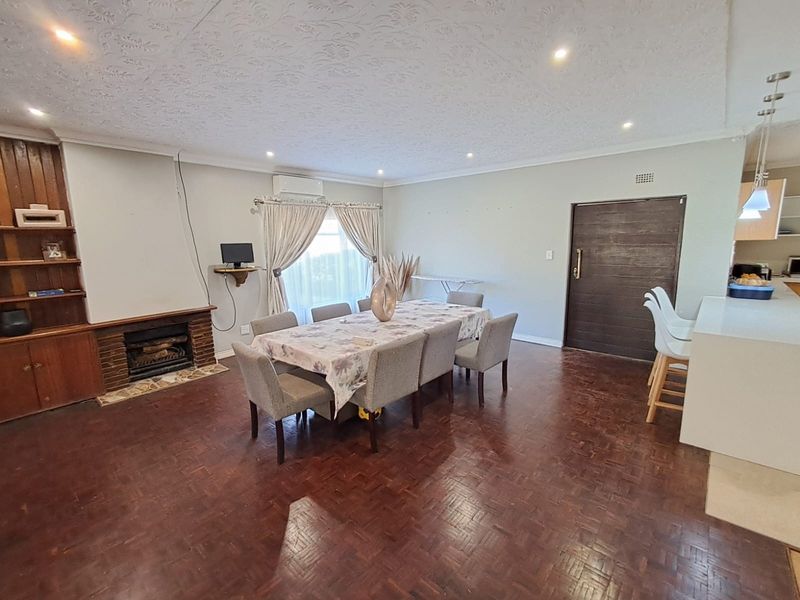 Spacious open-plan living and dining area featuring classic parquet flooring, a brick fireplace with built-in shelving, and a breakfast bar adjacent to the kitchen.