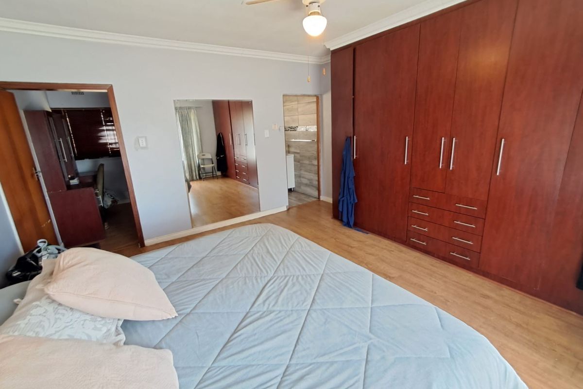 Spacious bedroom featuring extensive built-in wooden cabinetry, laminate flooring, a ceiling fan, and an integrated mirrored wall panel.