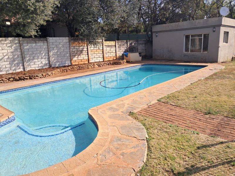 Outdoor pool area featuring a swimming pool with crazy paving surround, concrete block boundary wall, and a detached outbuilding.