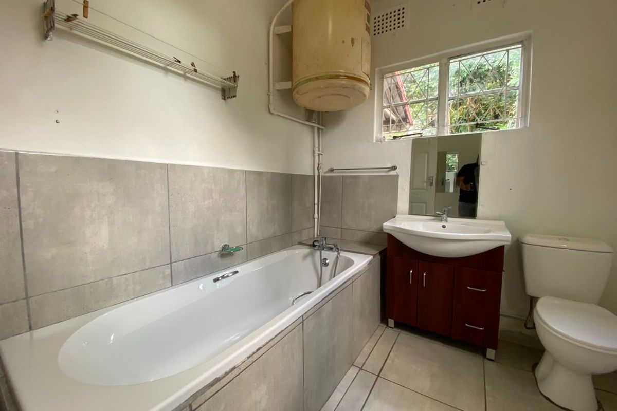 A functional bathroom featuring a bathtub, vanity unit, and toilet, with tiled finishes and an exposed electric water heater.