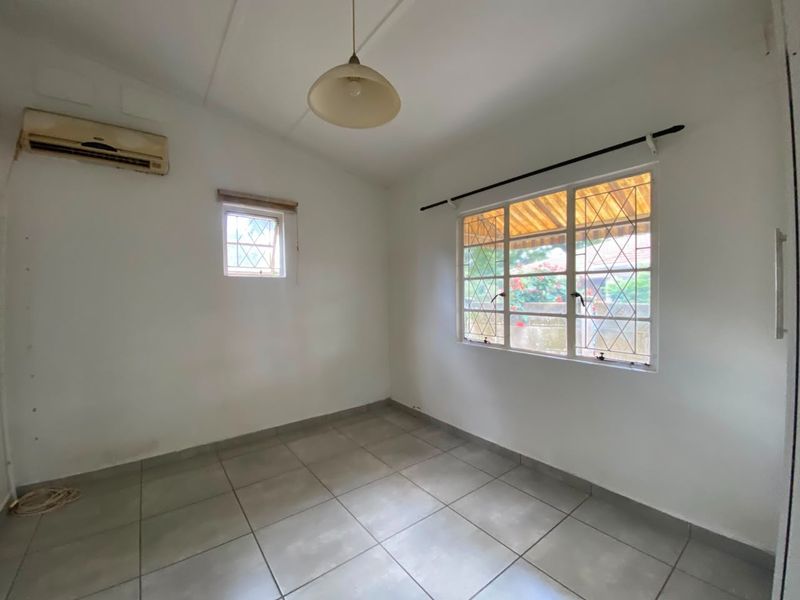 A vacant bedroom featuring tiled flooring, security bars on windows, and a wall-mounted air conditioning unit.