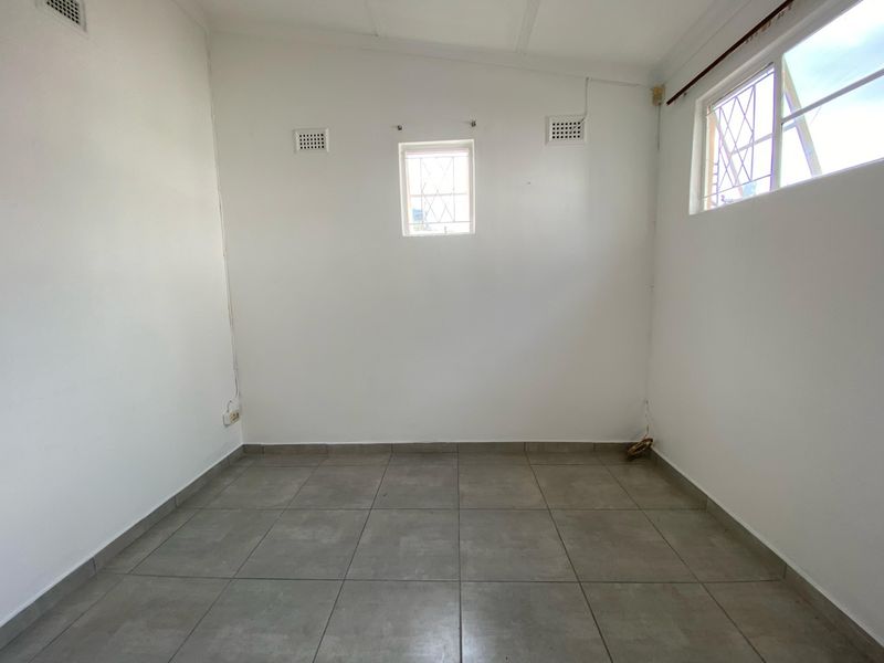 A vacant bedroom featuring neutral tiled flooring, multiple windows with security bars, and wall-mounted ventilation grilles.