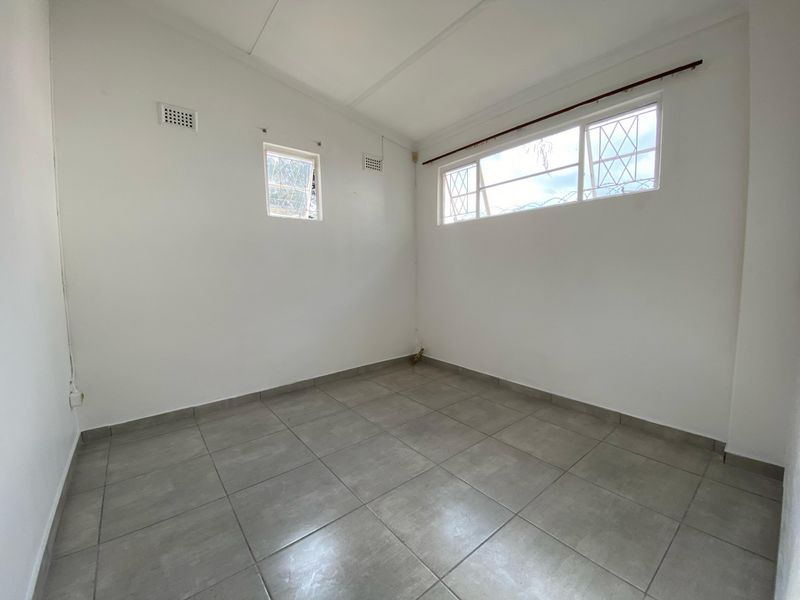 A clean, empty bedroom featuring neutral tiled flooring, white walls, and windows fitted with security bars.