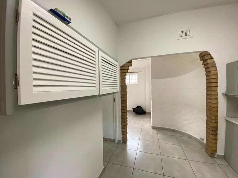 A functional hallway featuring a distinctive brick archway, neutral ceramic floor tiles, and built-in louvered cabinetry for storage.