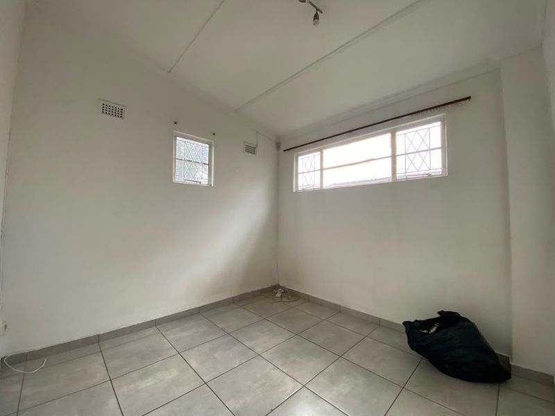 An empty bedroom featuring tiled flooring, security bars on the windows, and ventilation bricks, offering a blank canvas for renovation.