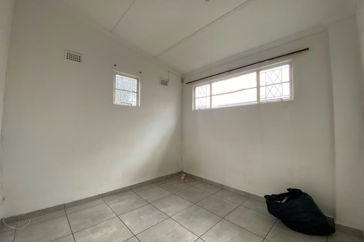 An empty bedroom featuring tiled flooring, security bars on the windows, and ventilation bricks, offering a blank canvas for renovation.