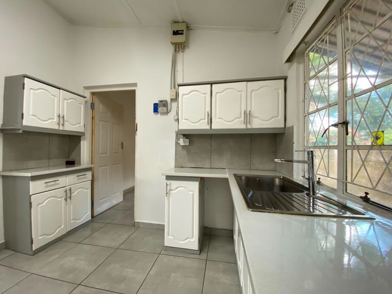 A functional kitchen featuring white cabinetry, tiled flooring, a stainless steel sink, and a window with security bars.