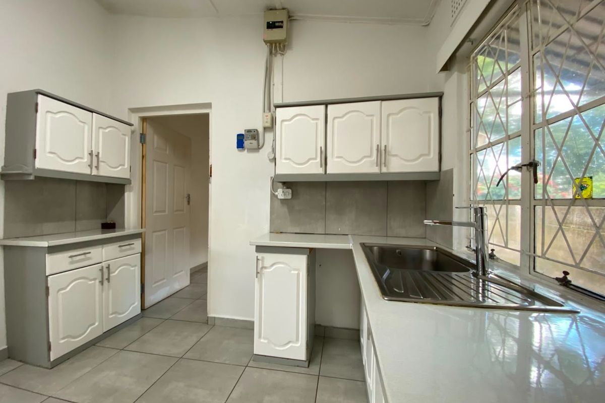 A functional kitchen featuring white cabinetry, tiled flooring, a stainless steel sink, and a window with security bars.