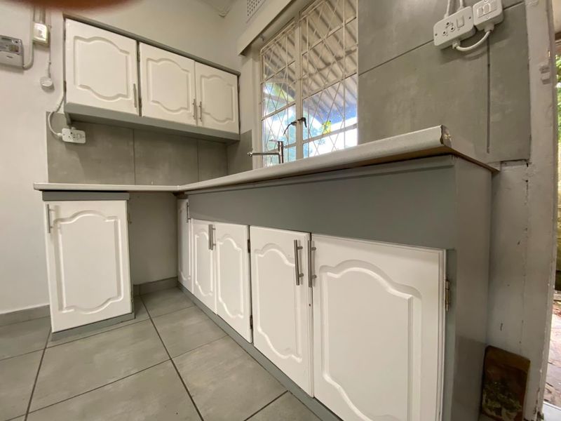 A compact kitchen featuring white cabinetry, grey tiled splashbacks, and a stainless steel sink with a mixer tap.