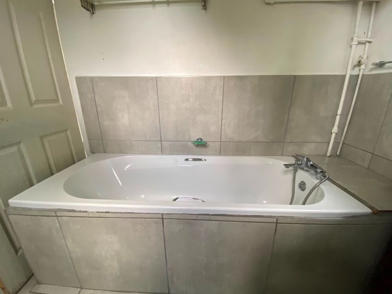 A functional bathroom featuring a built-in bathtub with grey tiled surround and exposed plumbing fixtures.