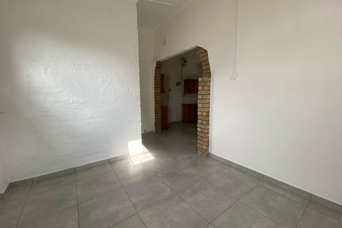 An empty living area featuring tiled flooring and a distinctive exposed brick archway leading to the kitchen space.