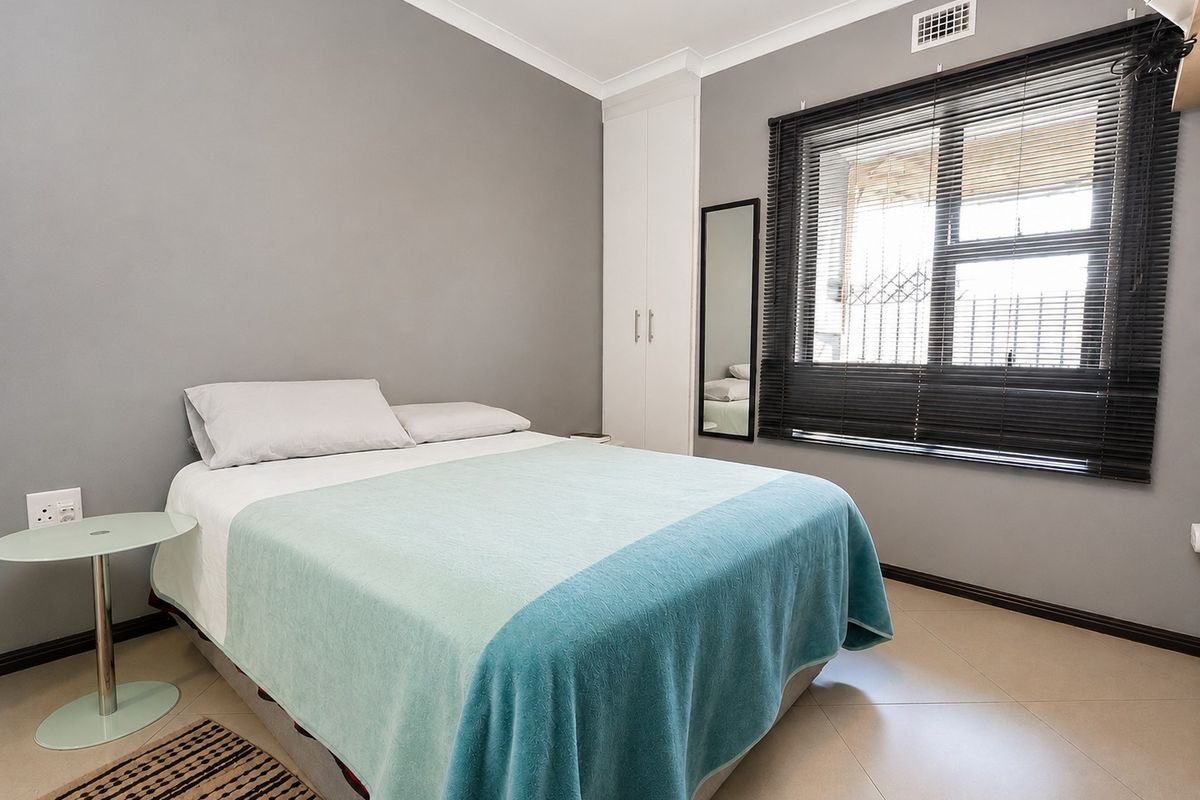 A well-maintained bedroom featuring neutral grey walls, tiled flooring, a built-in wardrobe, and an air conditioning vent.