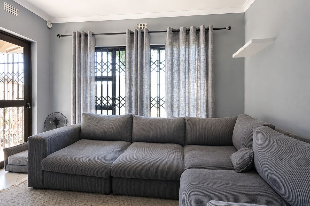 A well-maintained living room featuring neutral grey walls, decorative cornicing, and security gates on the windows and door.