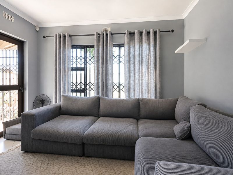 A well-maintained living room featuring neutral grey walls, decorative cornicing, and security gates on the windows and door.