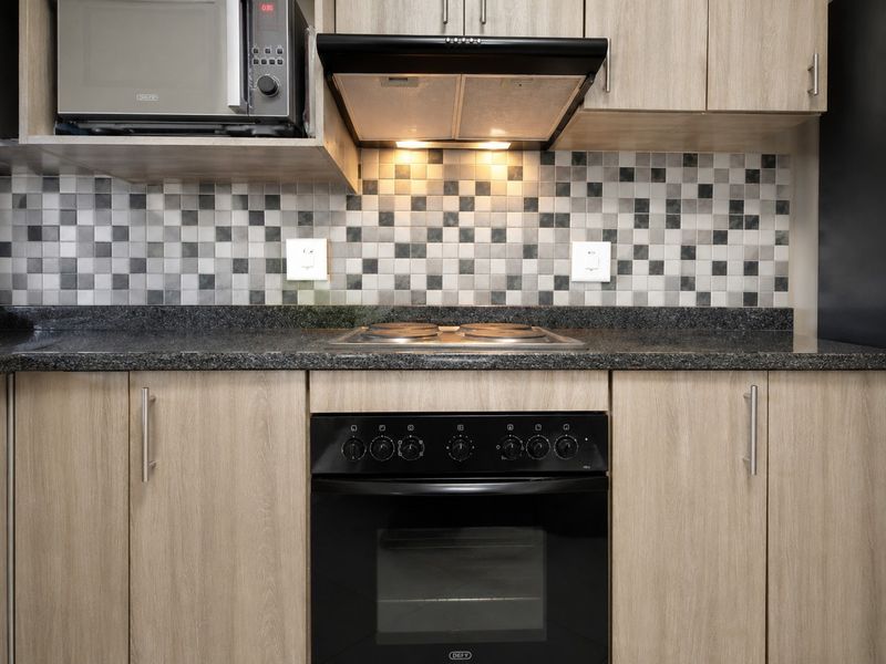 A modern kitchen featuring light wood cabinetry, granite countertops, a mosaic tile backsplash, and integrated appliances including an oven, hob, and extractor fan.