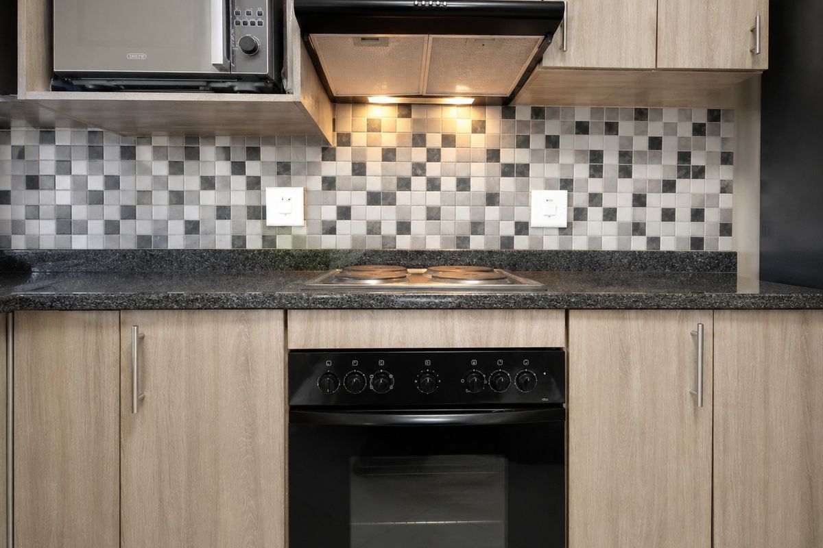A modern kitchen featuring light wood cabinetry, granite countertops, a mosaic tile backsplash, and integrated appliances including an oven, hob, and extractor fan.