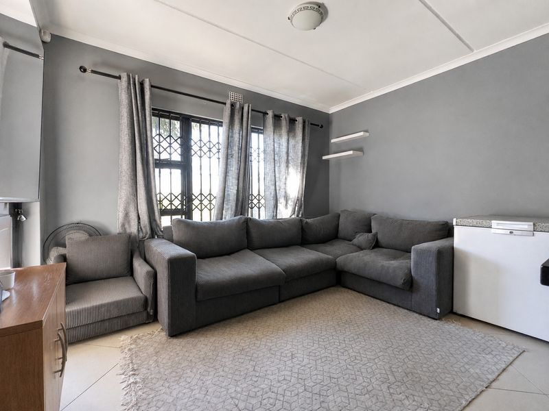 A living room featuring grey walls, tiled flooring, and a window fitted with a security gate.