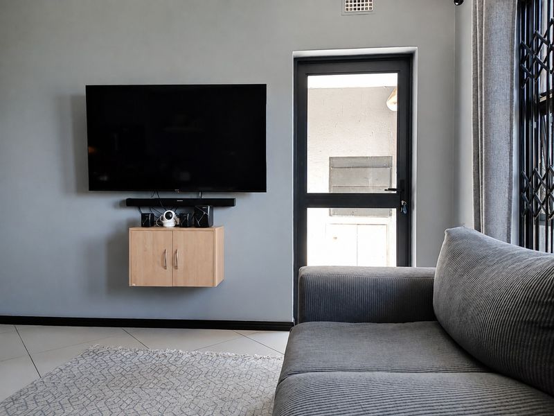 A modern living room featuring neutral grey walls, tiled flooring, and a wall-mounted storage cabinet with direct access to an outdoor area.