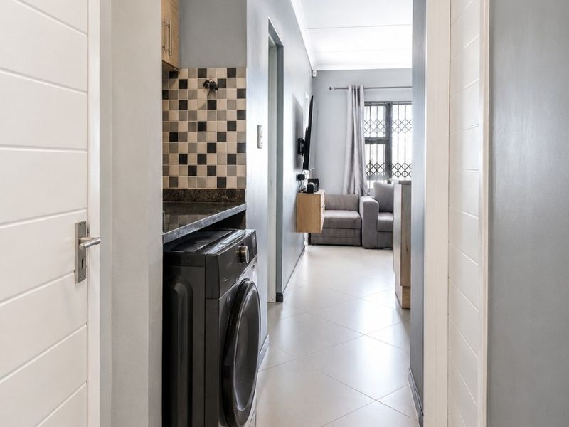 A well-lit hallway featuring tiled flooring, built-in cabinetry with a stone countertop, and a tiled splashback, leading towards the living area.